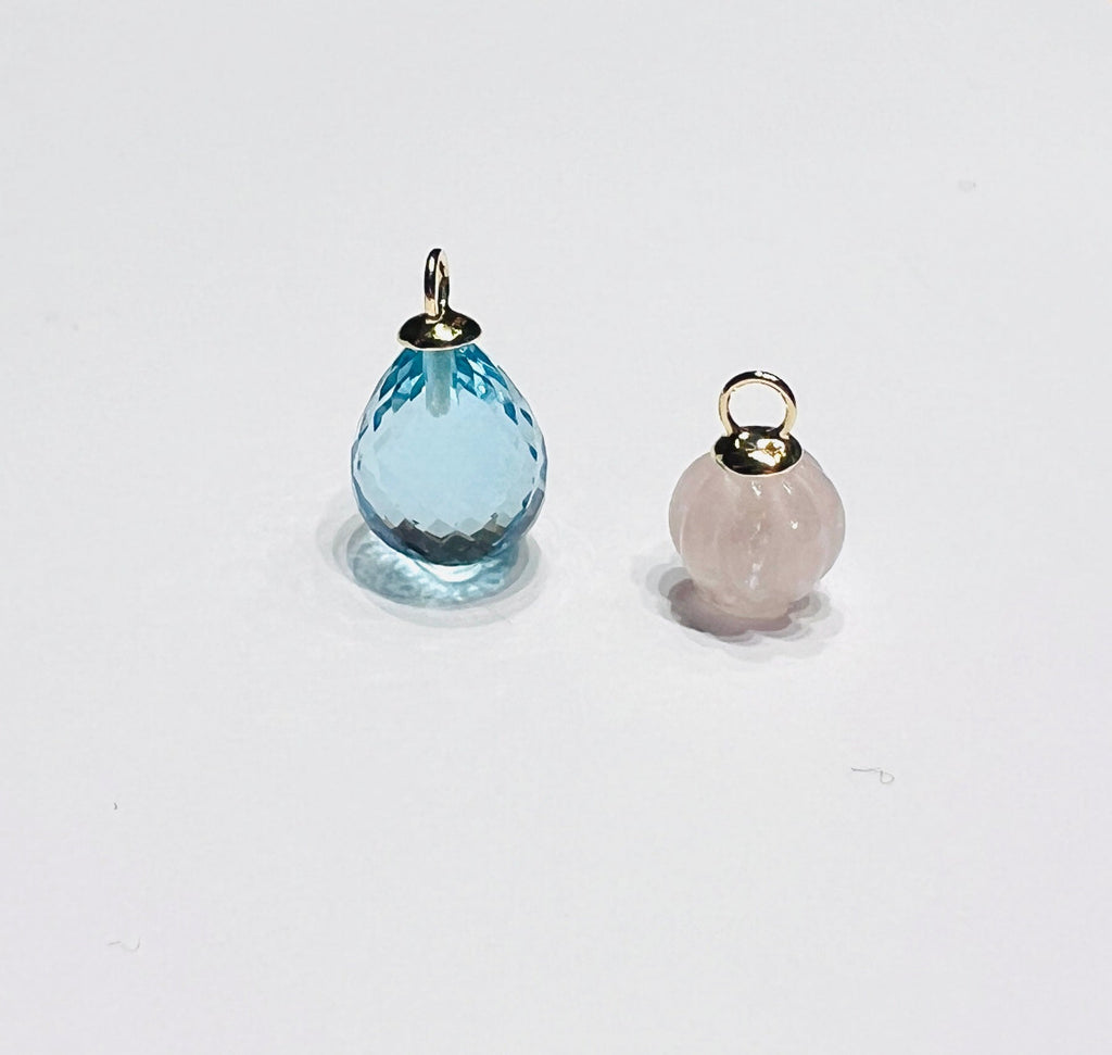 Atelier Beatrix Wolter-Anhänger  aus facettiertem himmelblauen Topas in Tropfenform  mit einer Anhängerkappe und Öse aus 750 Gold. Neben einem Anhänger aus gravierter Rosenquarz in Pumpkinform mit Anhängerkappe und Öse aus 750 Gold I 18K Gold.